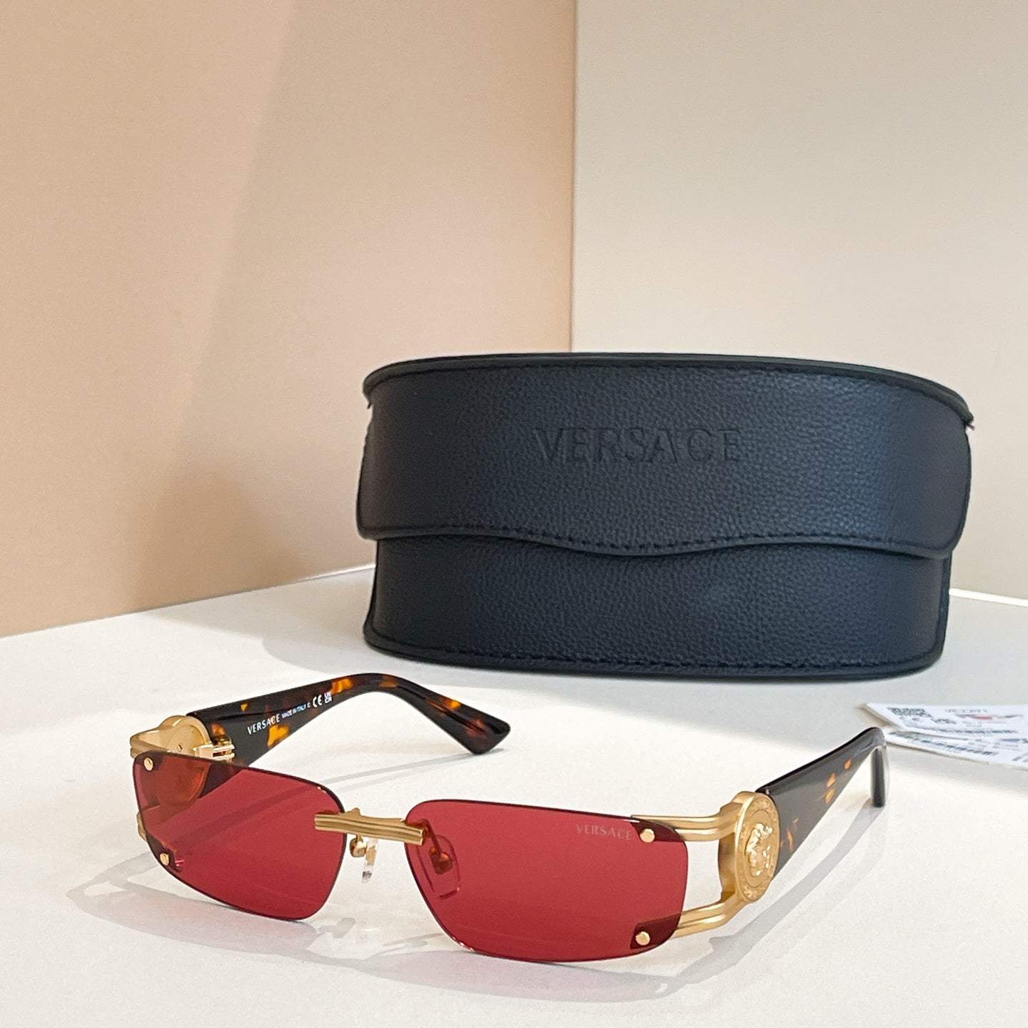 Red-lens sunglasses with gold frames and black case behind