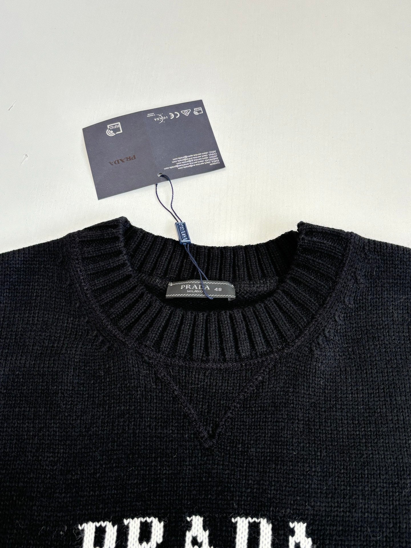 Black crewneck sweater neckline with neck tag and partial PRADA lettering