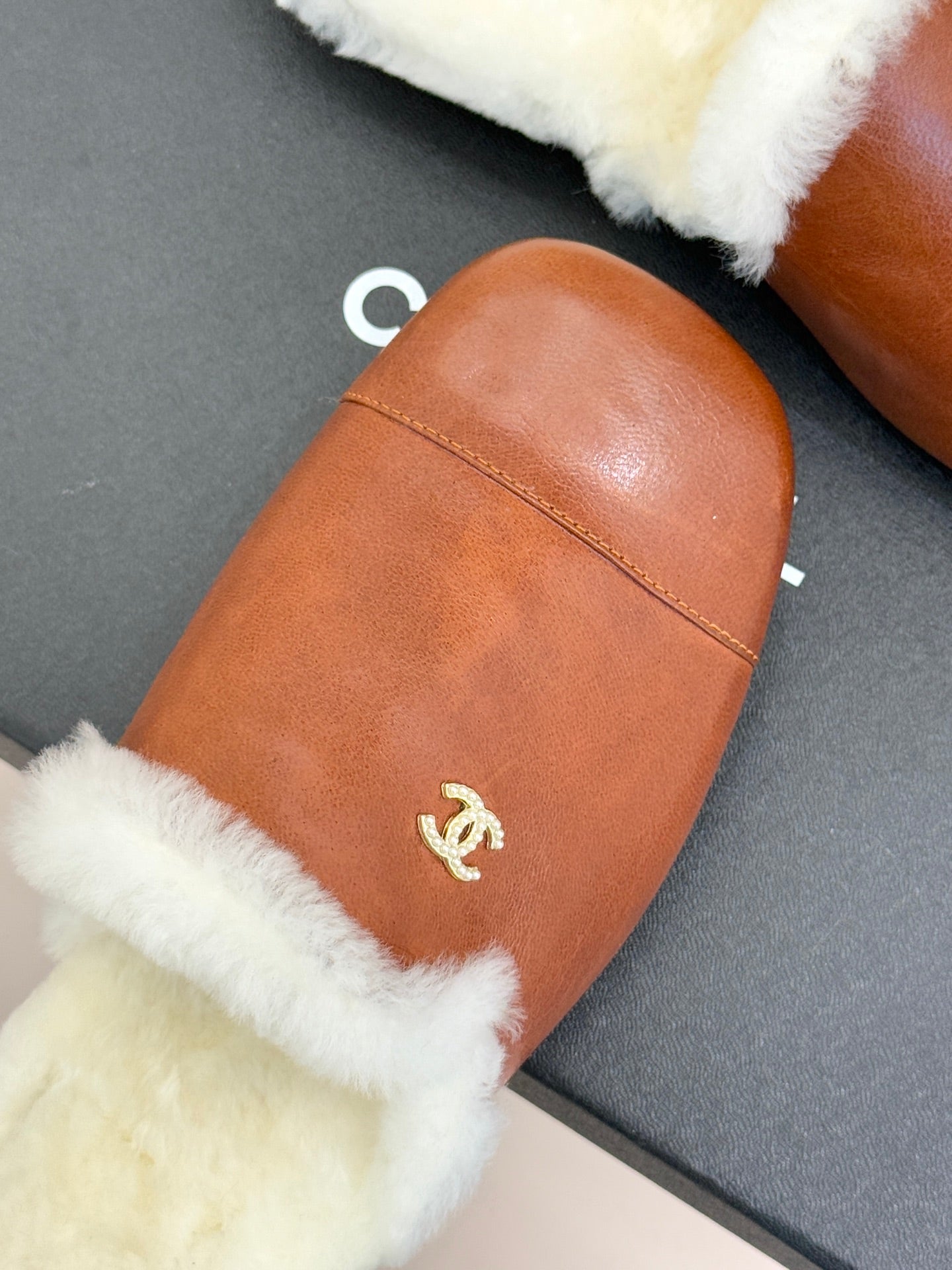 Close-up brown leather mule slipper with white shearling edge and gold Chanel logo