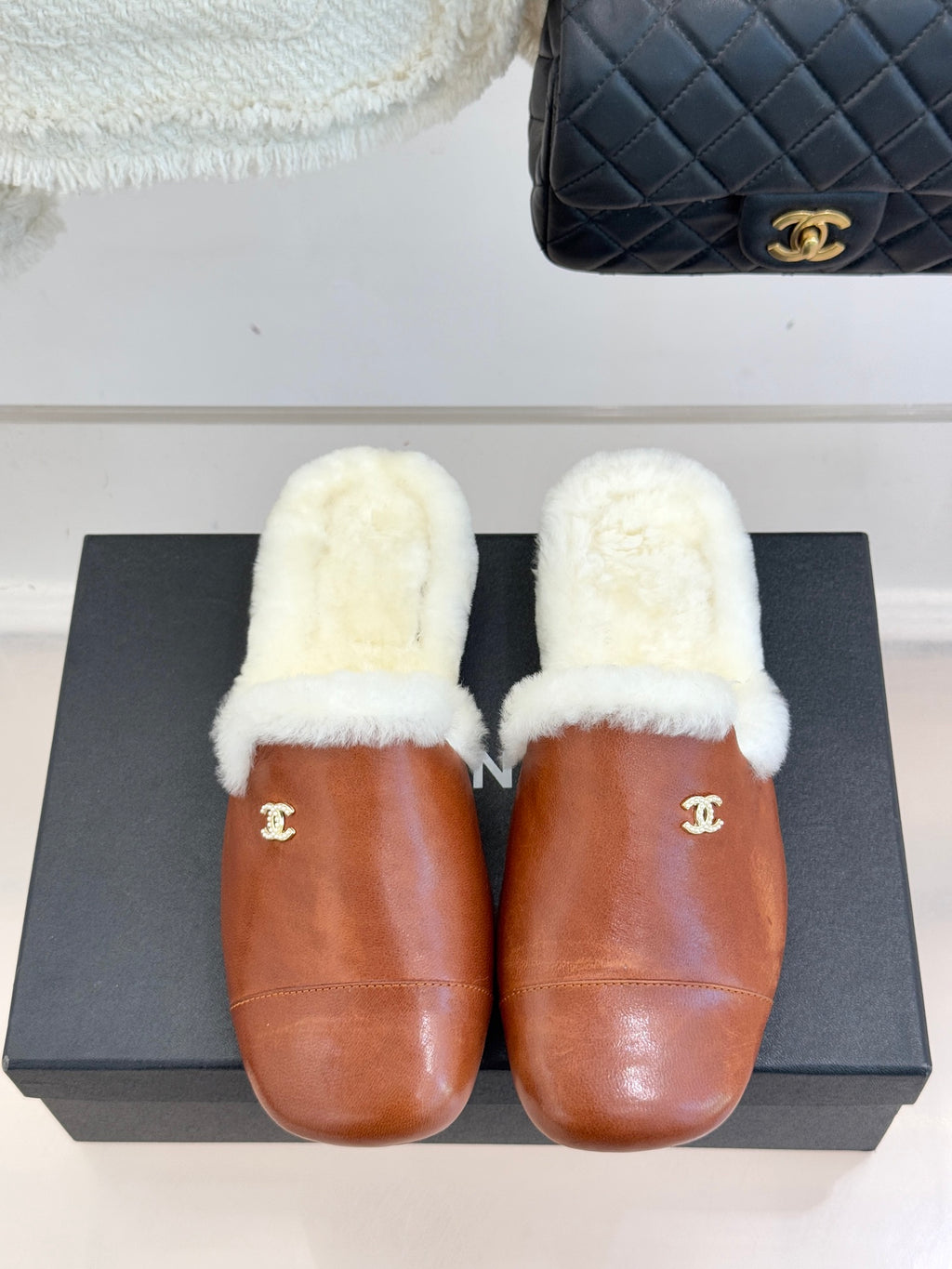 Brown leather mule slippers with white shearling uppers and gold Chanel emblem