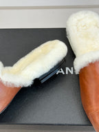 Brown leather mule with white shearling lining on a dark shoe box