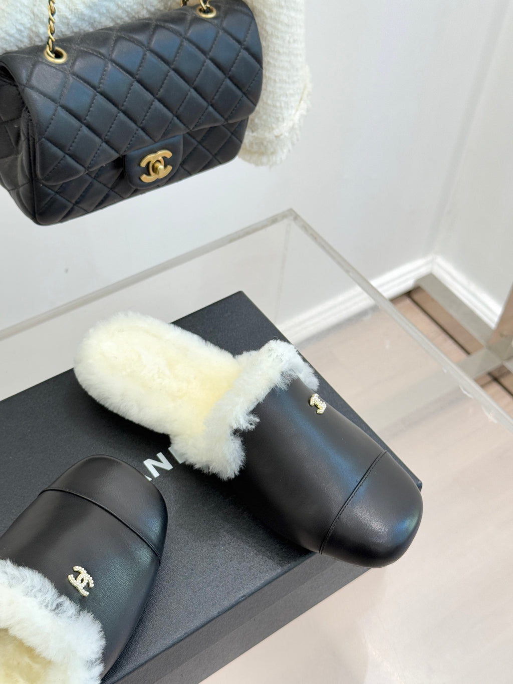 Black leather mules with white shearling trim on display with quilted bag