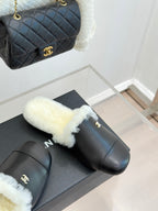Black leather mules with white shearling trim on display with quilted bag