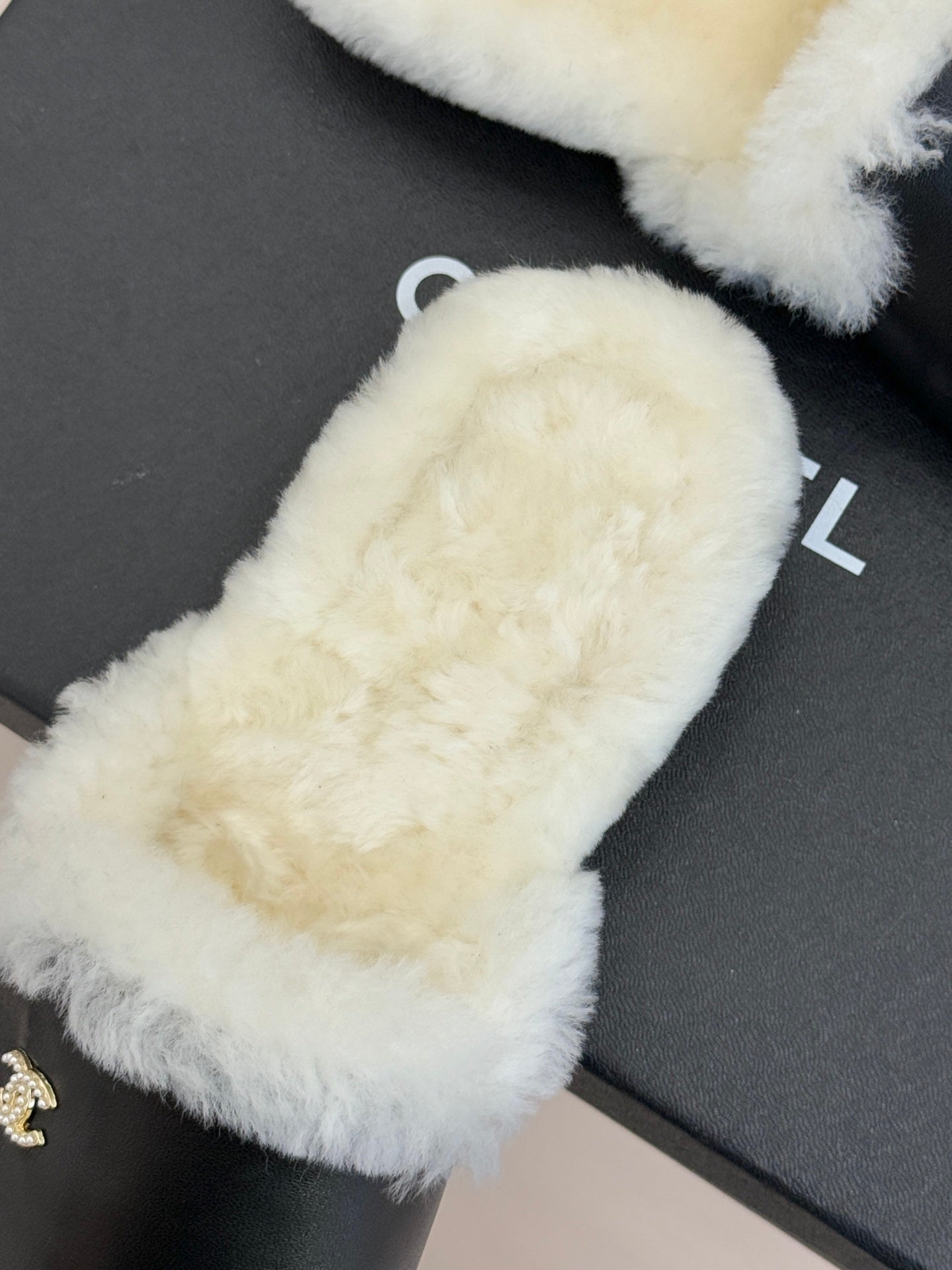 Close-up of white fur-trimmed black mules with gold logo on toe area