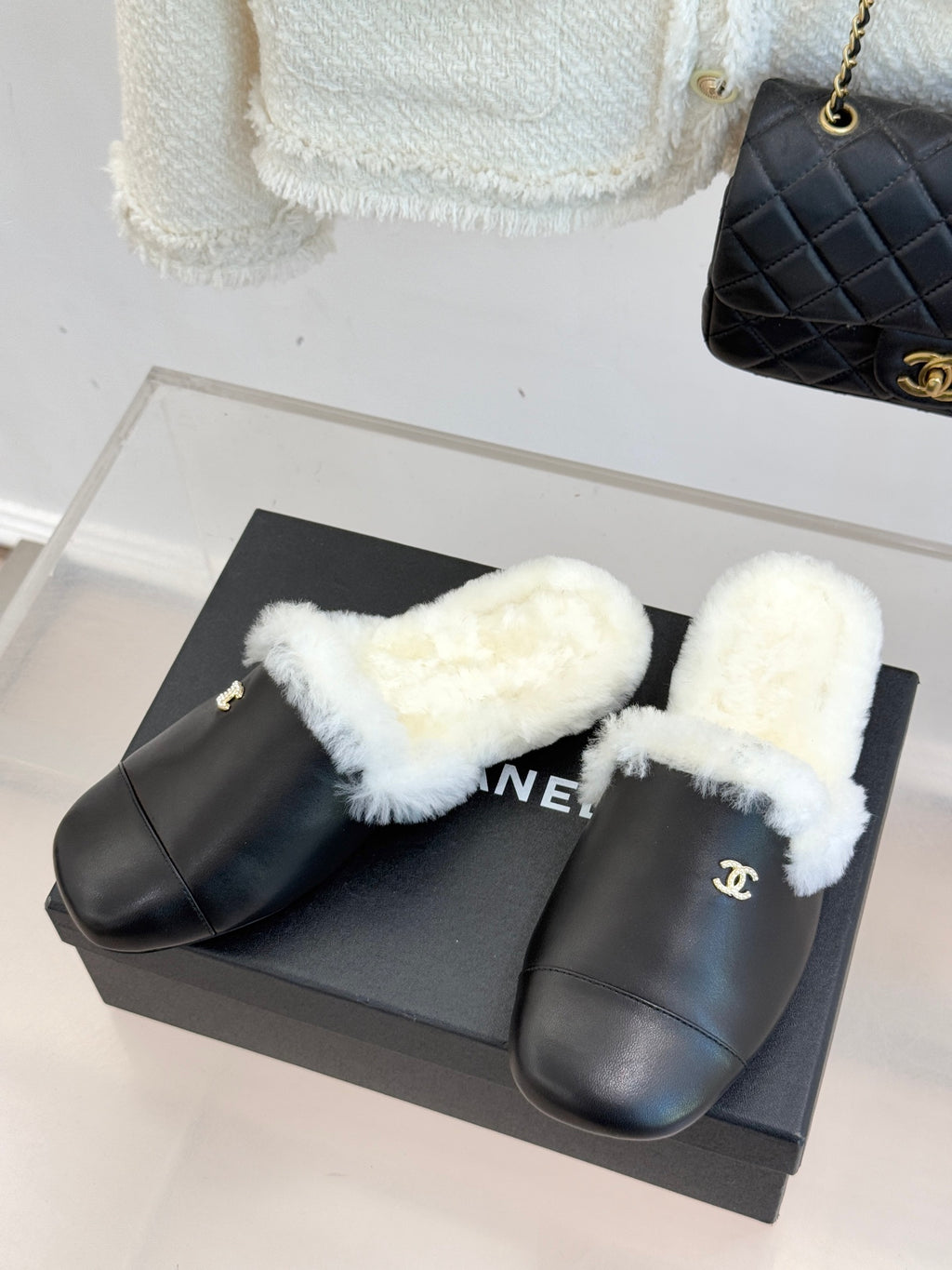 Pair of black leather mules with white plush shearling straps on a box