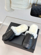 Pair of black leather mules with white plush shearling straps on a box