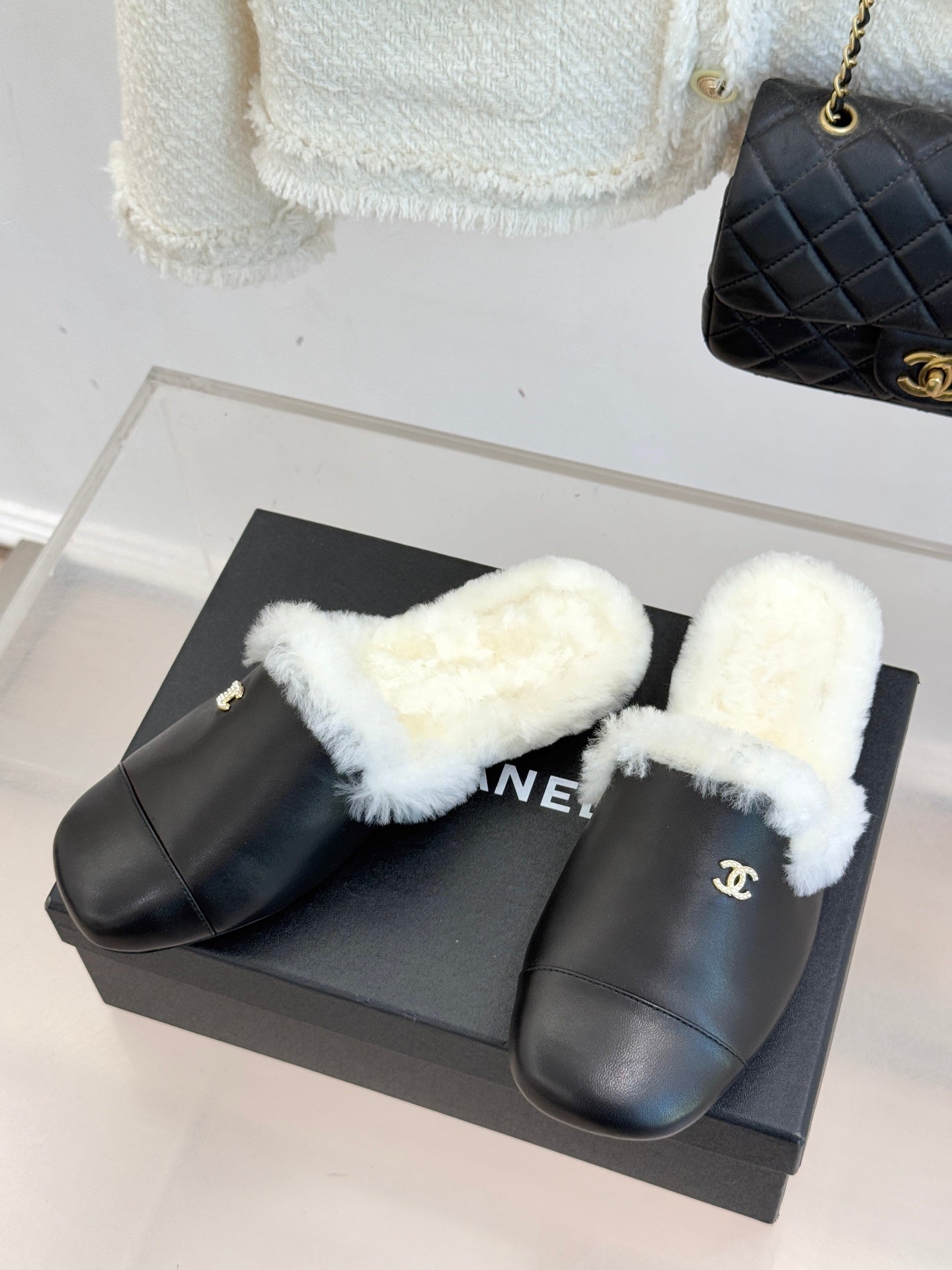 Pair of black leather mules with white plush shearling straps on a box