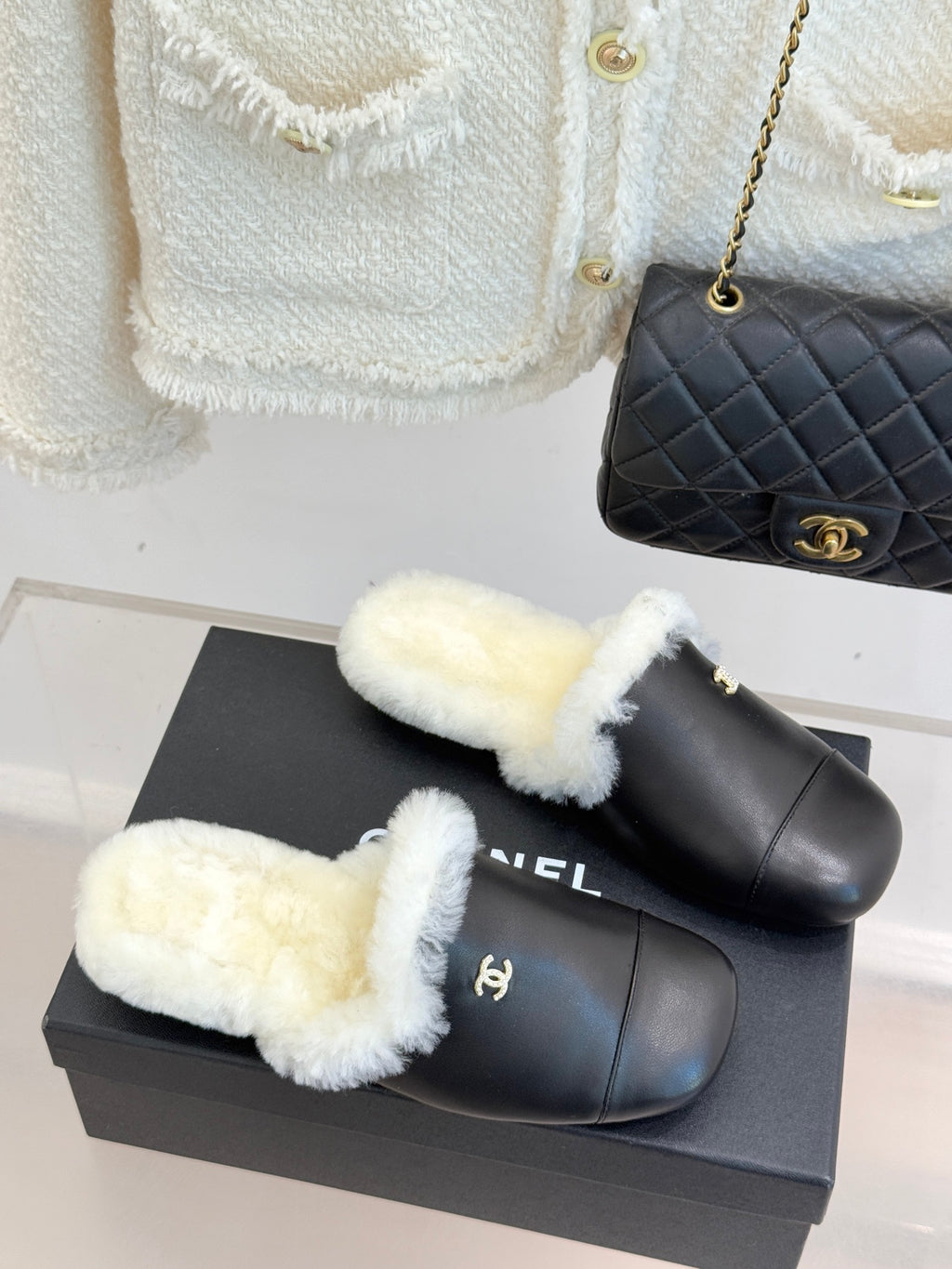Black leather mules with white shearling cuff straps and gold logo ornament