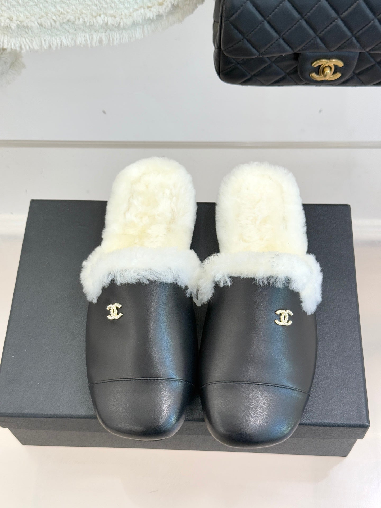 Black leather mules with white plush fur straps and gold logo emblem