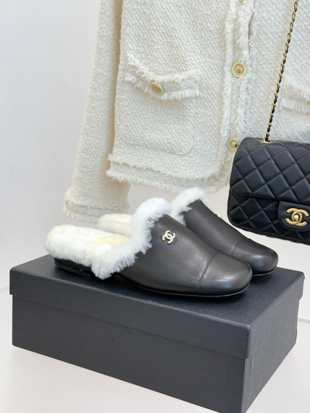 Black leather mules with white shearling crossover strap and gold logo detail
