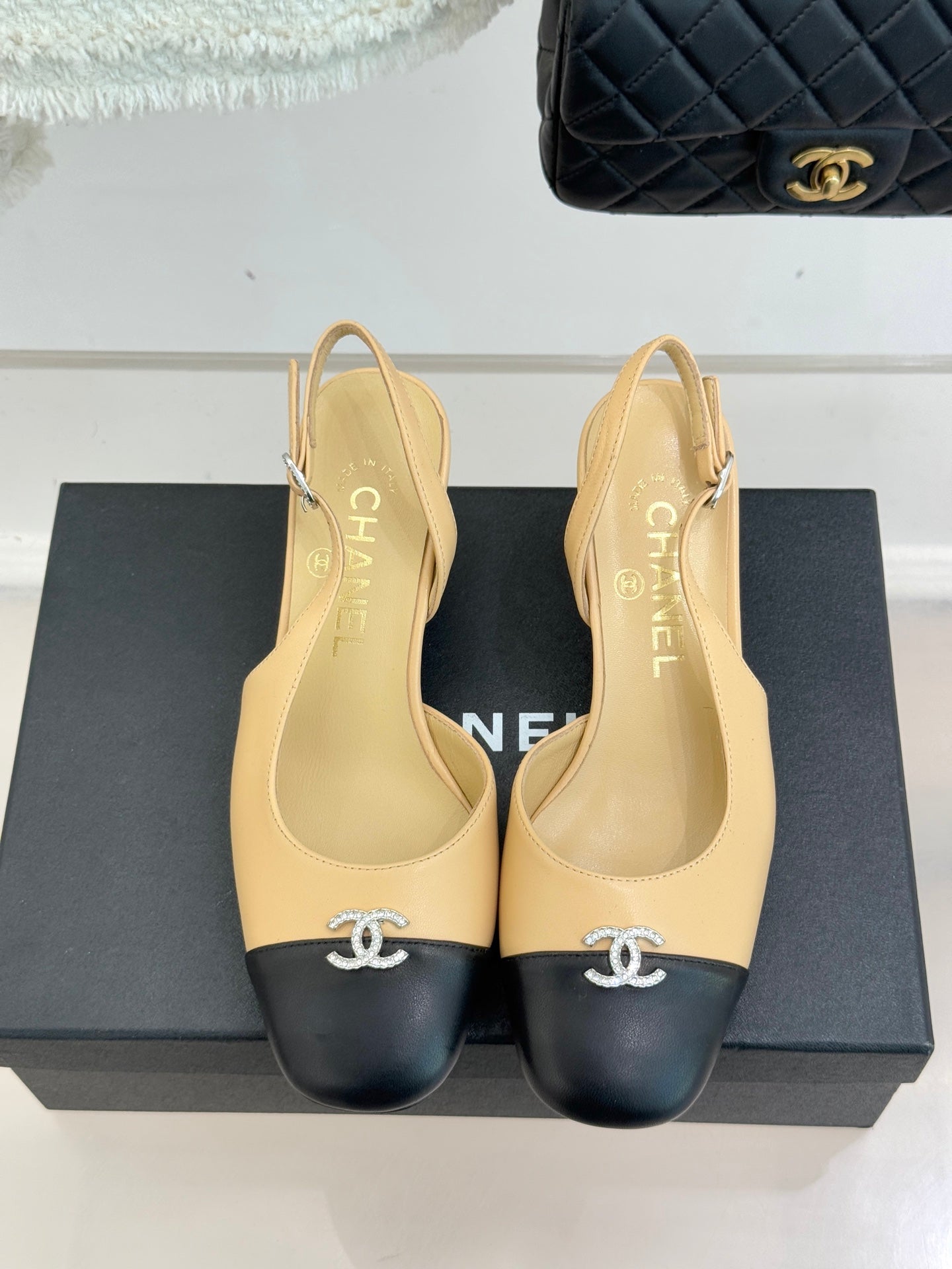 Women's Chanel slingback heels with beige uppers, black toe caps, CC emblem at front.
