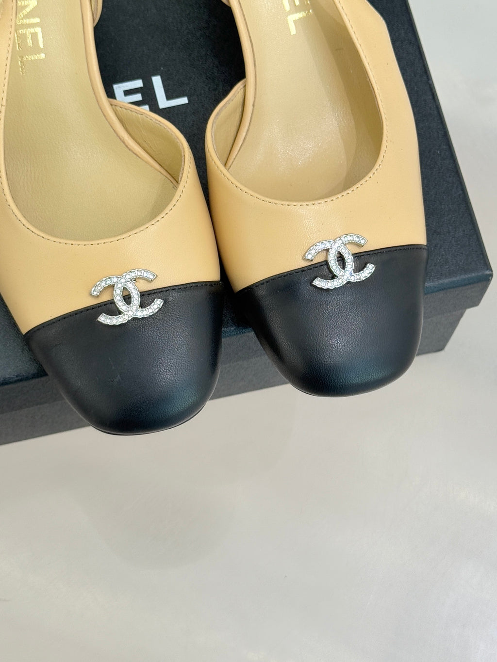 Women's Chanel slingback heels close-up, beige uppers, black toe caps, rhinestone CC.