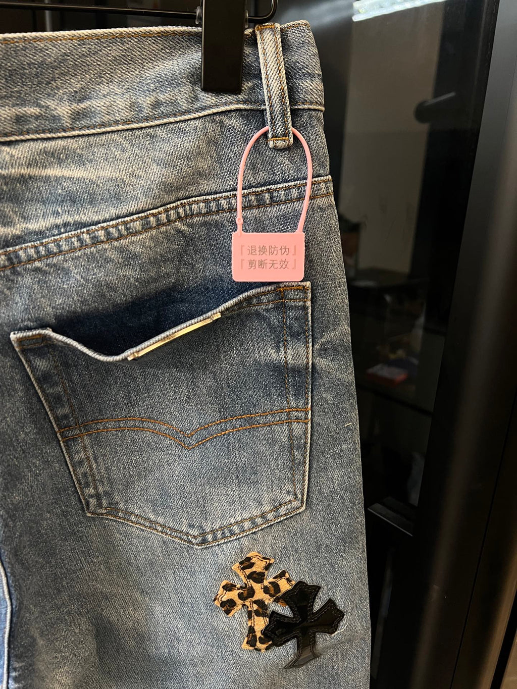 Light-wash denim pants with side pocket, gold cross patch, and hanging tag