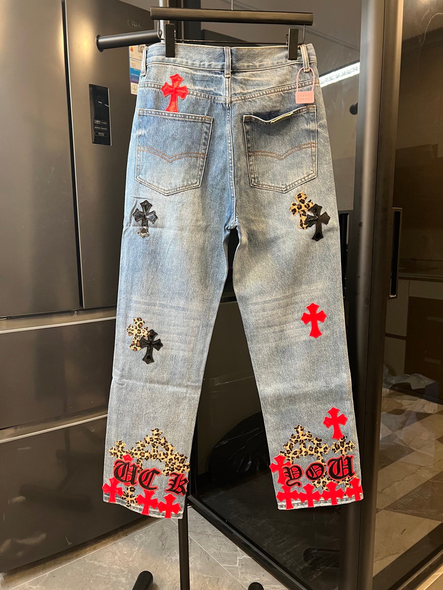 Light-wash denim pants with red and black cross patches, rear view and back pockets