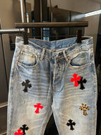 Light-wash denim pants with red and black cross patches on front legs, waistband view