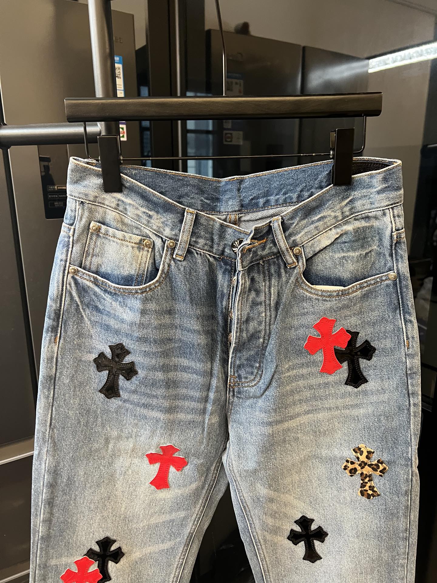 Light-wash denim pants with red and black cross patches on front legs, waistband view