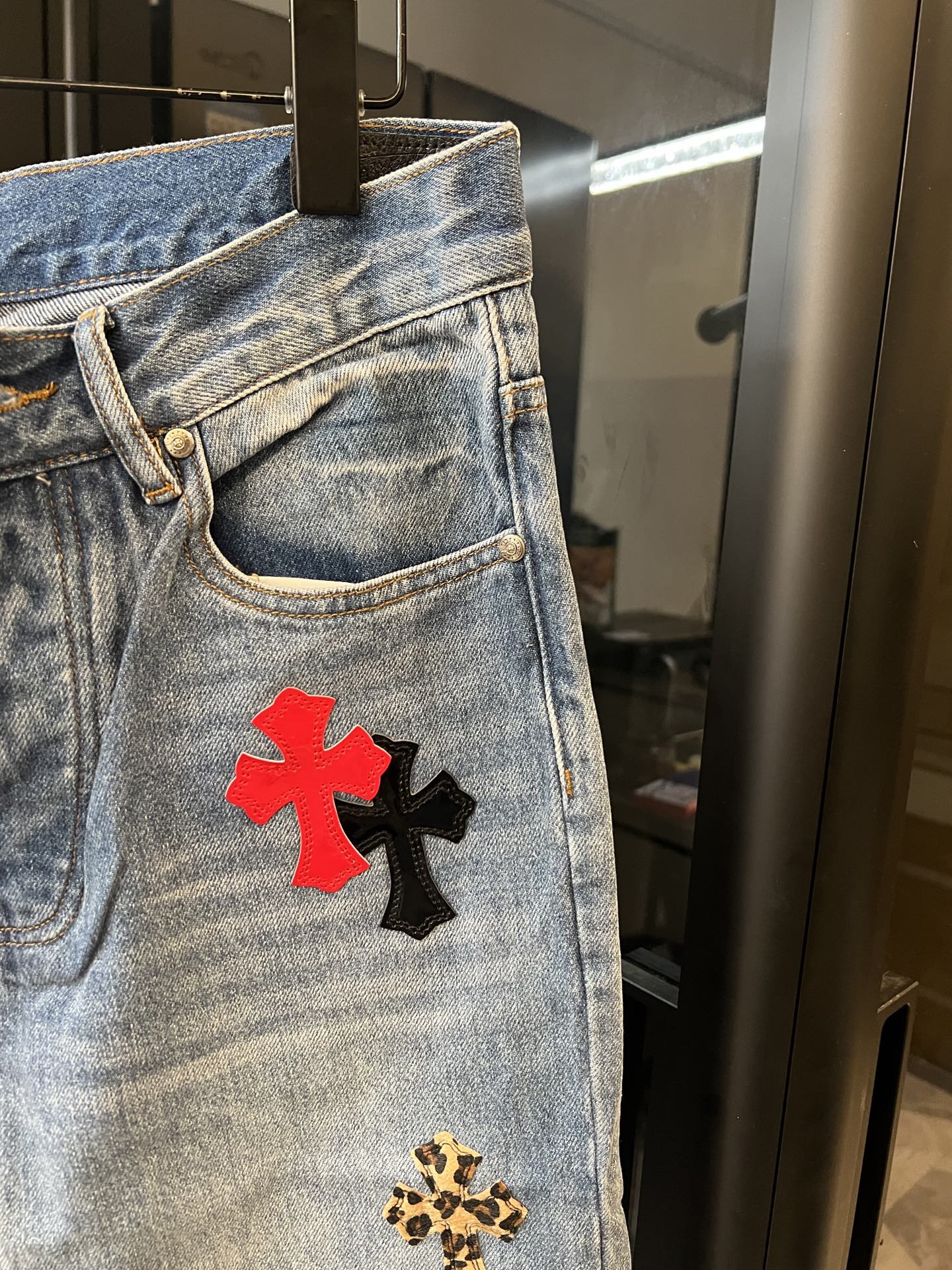 Light-wash denim pants front pocket with red cross patch and gold leopard cross