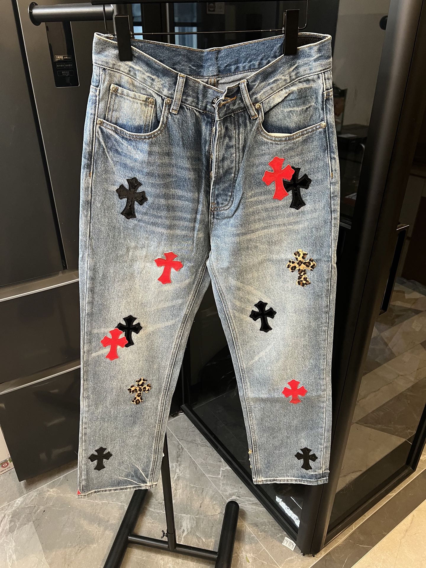 Light-wash denim pants with red, black, and gold cross patches, front view