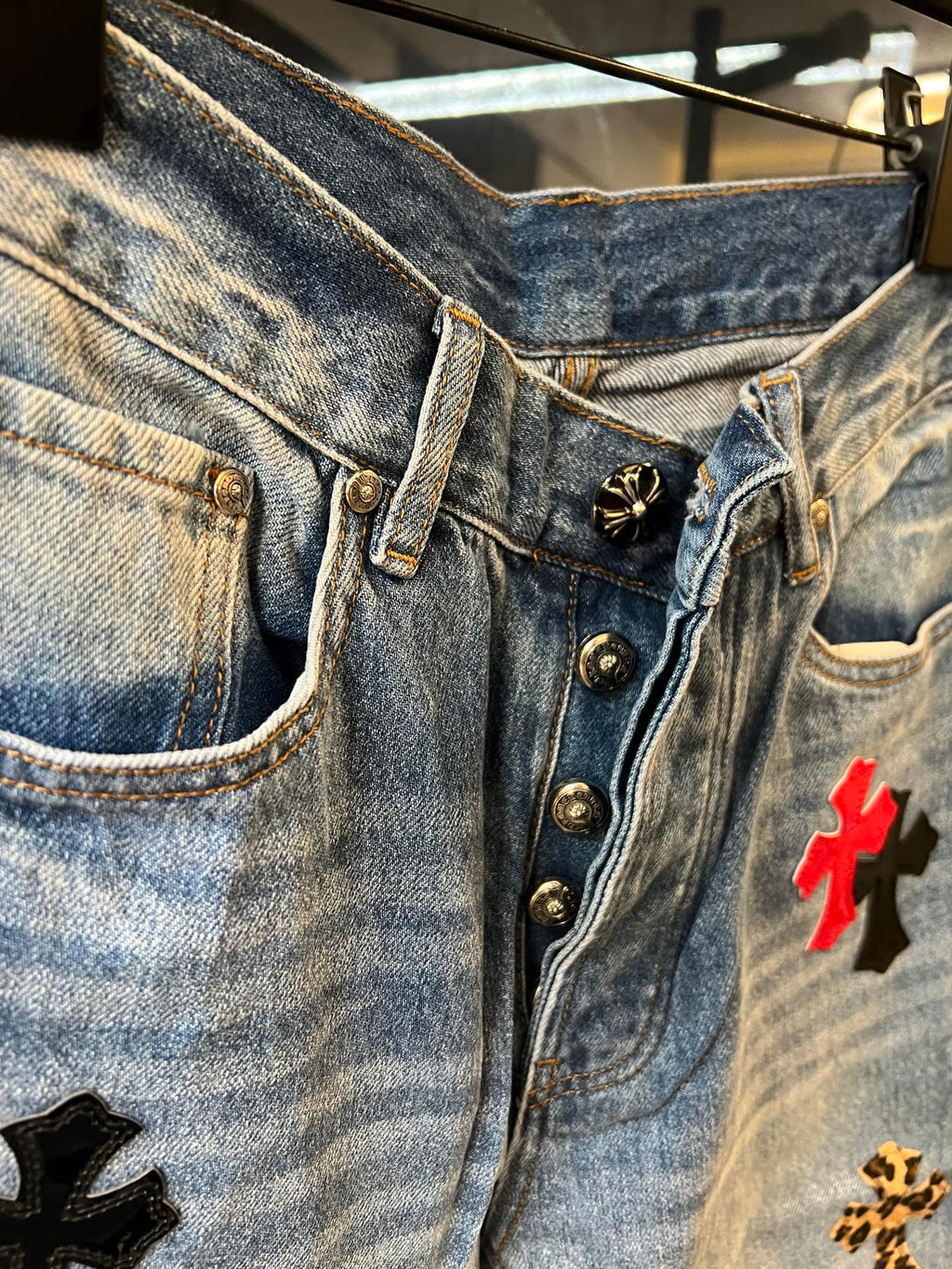 Light-wash denim pants with metal button closure and red cross patch, waistband close