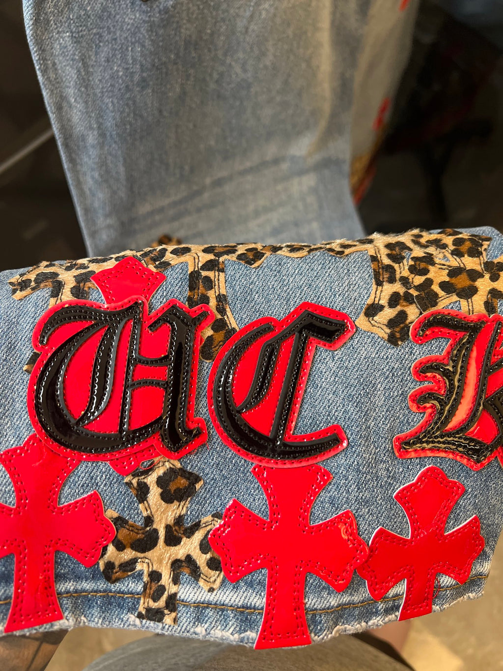 Light-wash denim cuff with leopard-print patch and red-and-black logo lettering