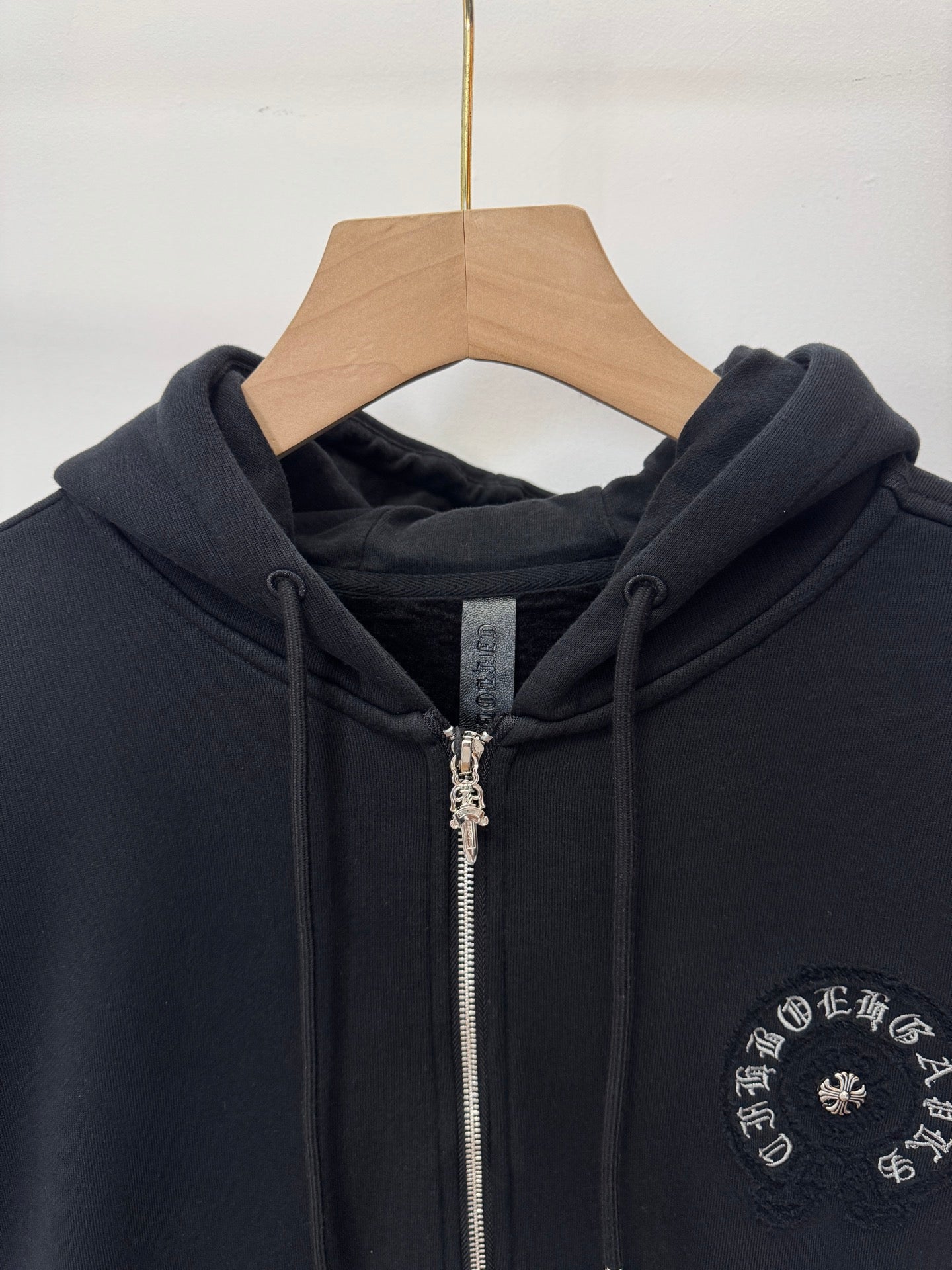 Black zip-up hoodie neckline and hood with drawstrings, zipper, and chest circular emblem.