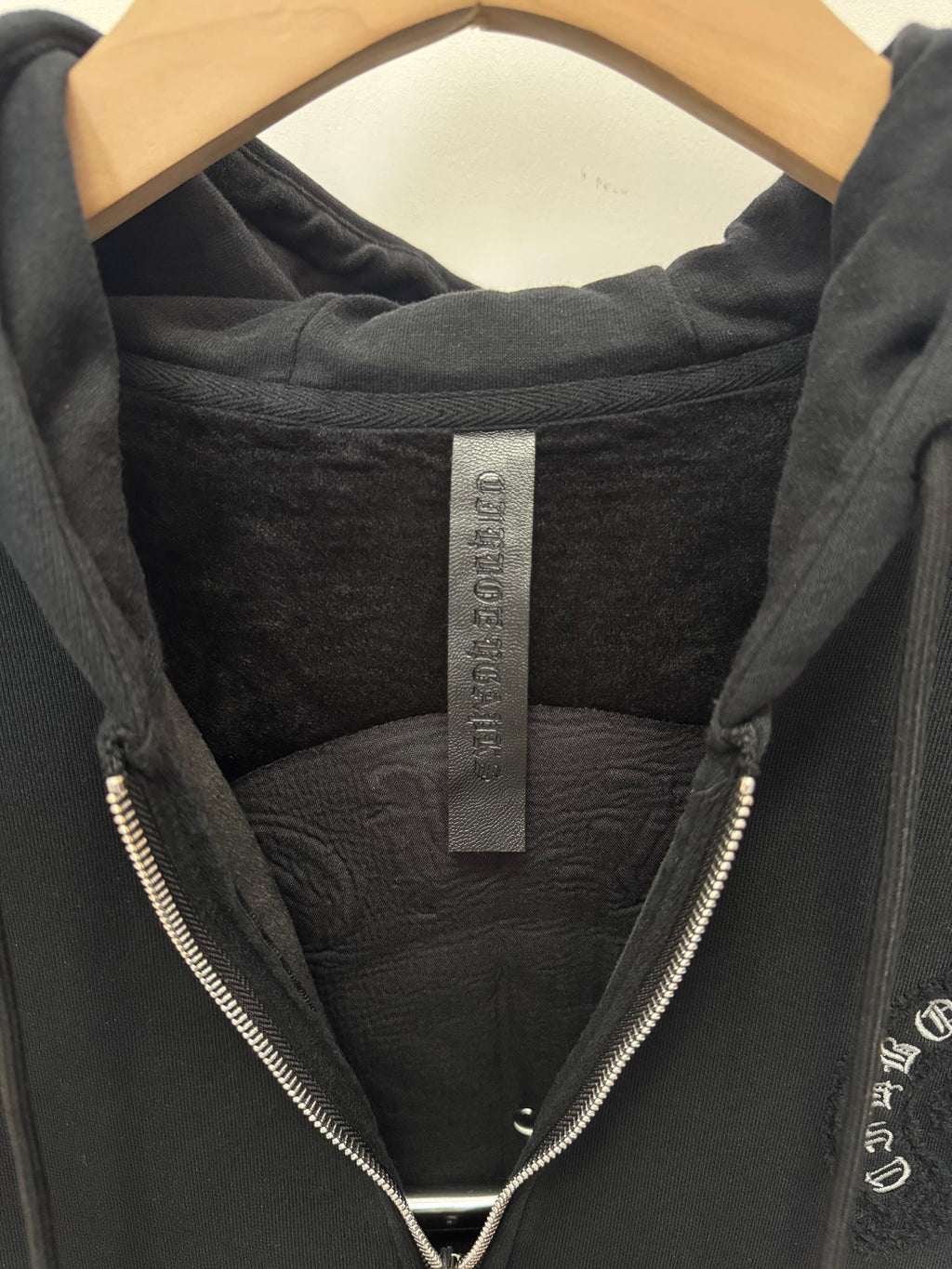 Black hoodie hood interior with brand label tag and front zipper teeth visible.