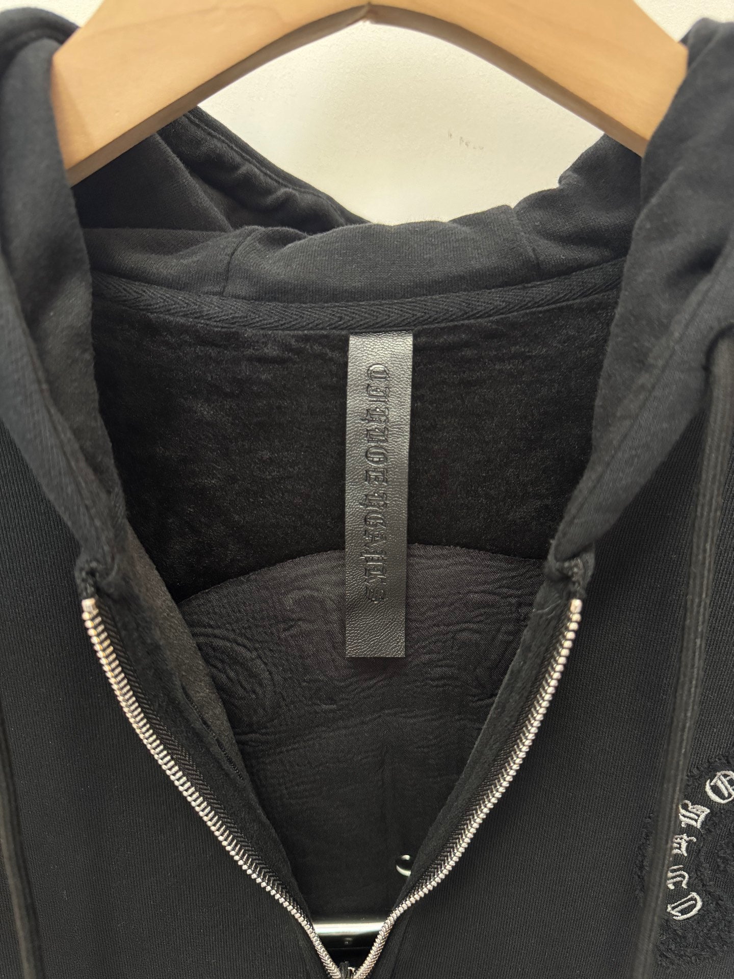Black hoodie hood interior with brand label tag and front zipper teeth visible.