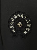 Embroidered circular patch on black hoodie, gold-toned symbols and small center flower.