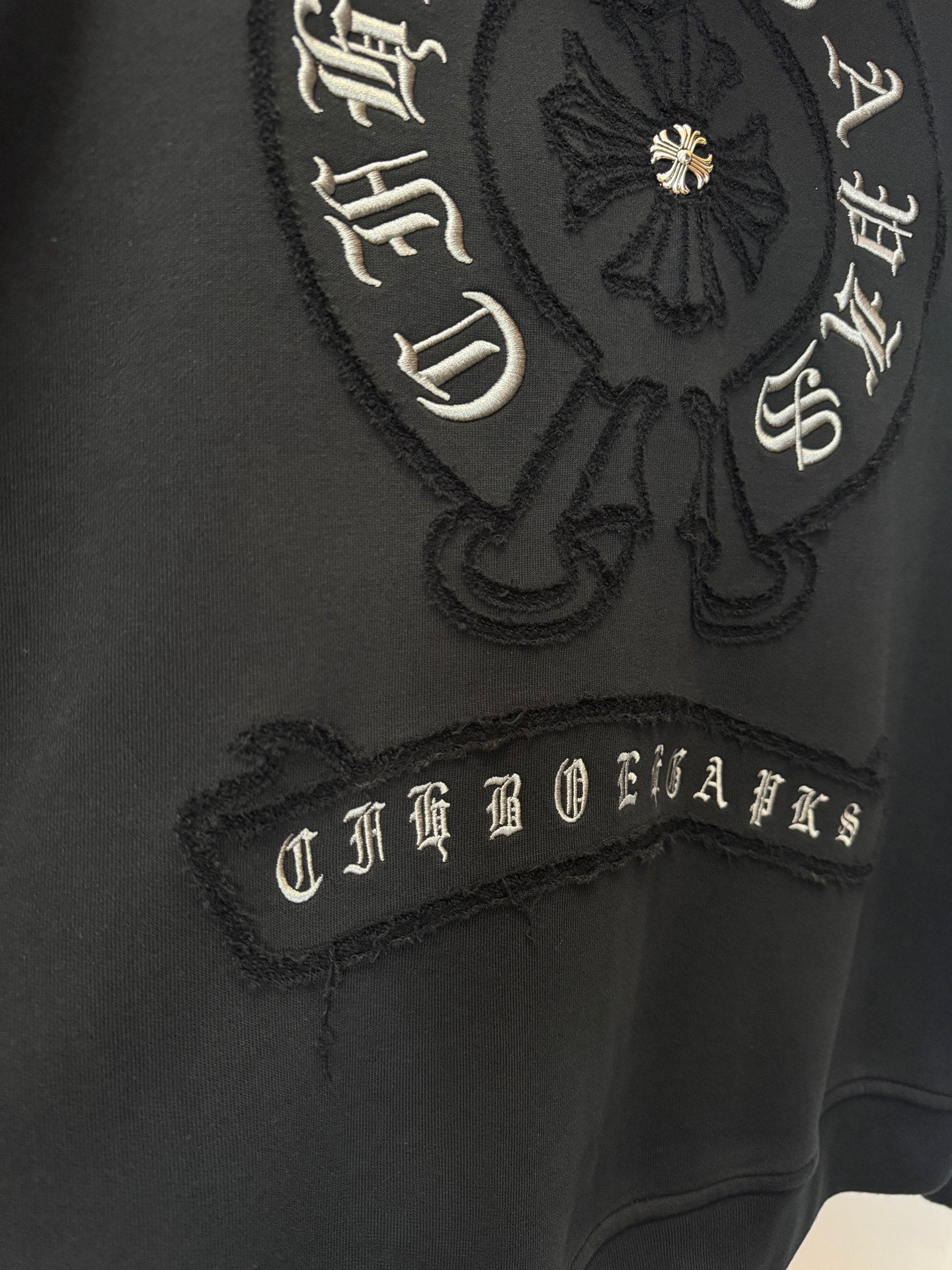 Black hoodie with embroidered crest and script lettering on the chest