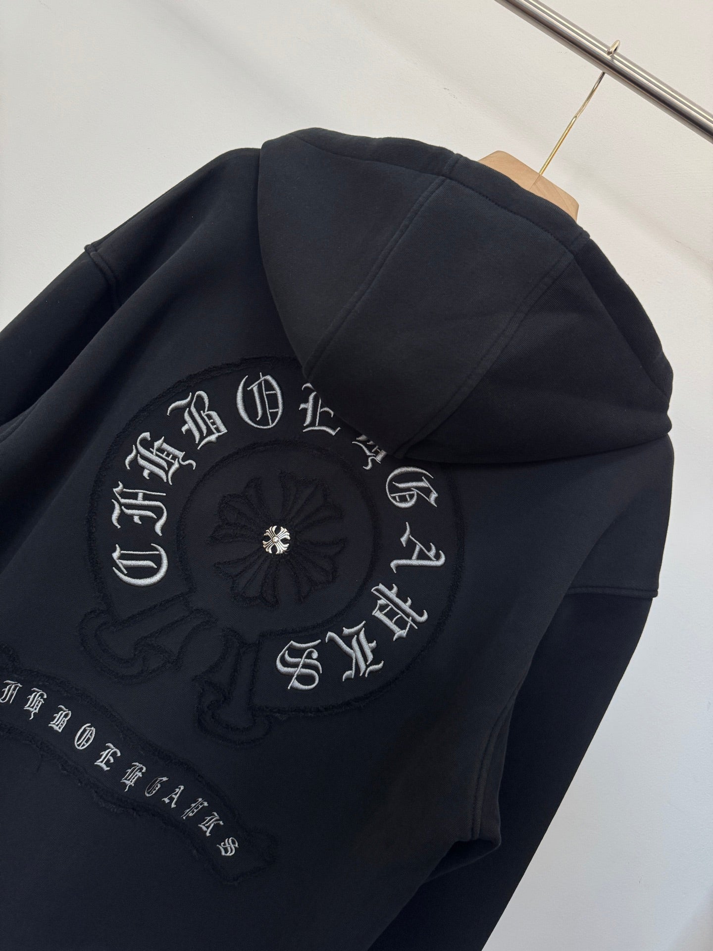 Black zip-up hoodie back detail with circular embroidery and decorative lettering.