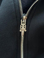 Close-up of metal zipper pull on black hoodie with stitched teeth and keychain-style charm.