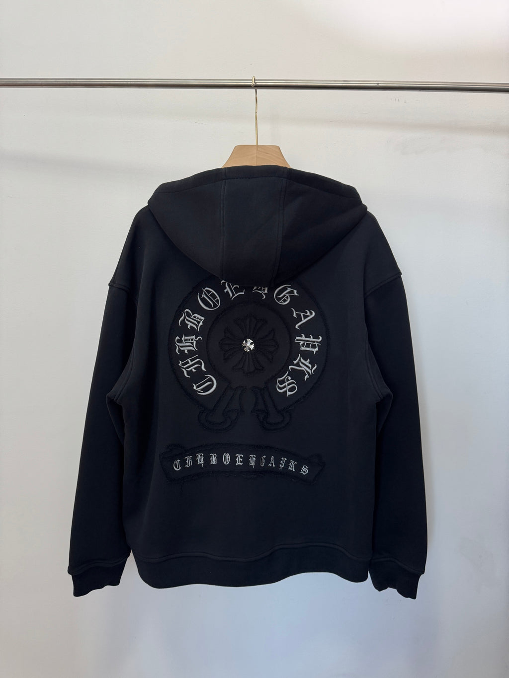 Black zip-up hoodie, back view with large circular embroidery and printed arch text.