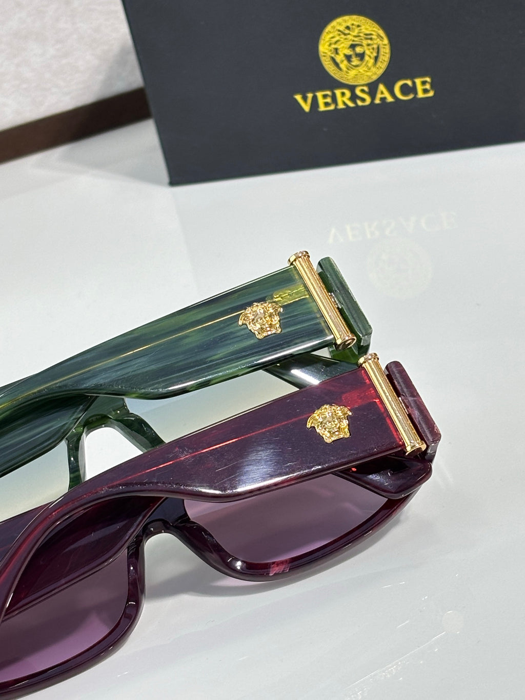 Versace sunglasses with green and purple frames, each with gold temple hardware