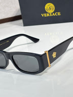 Versace sunglasses close-up with black frames and gold emblem on temples, dark lenses