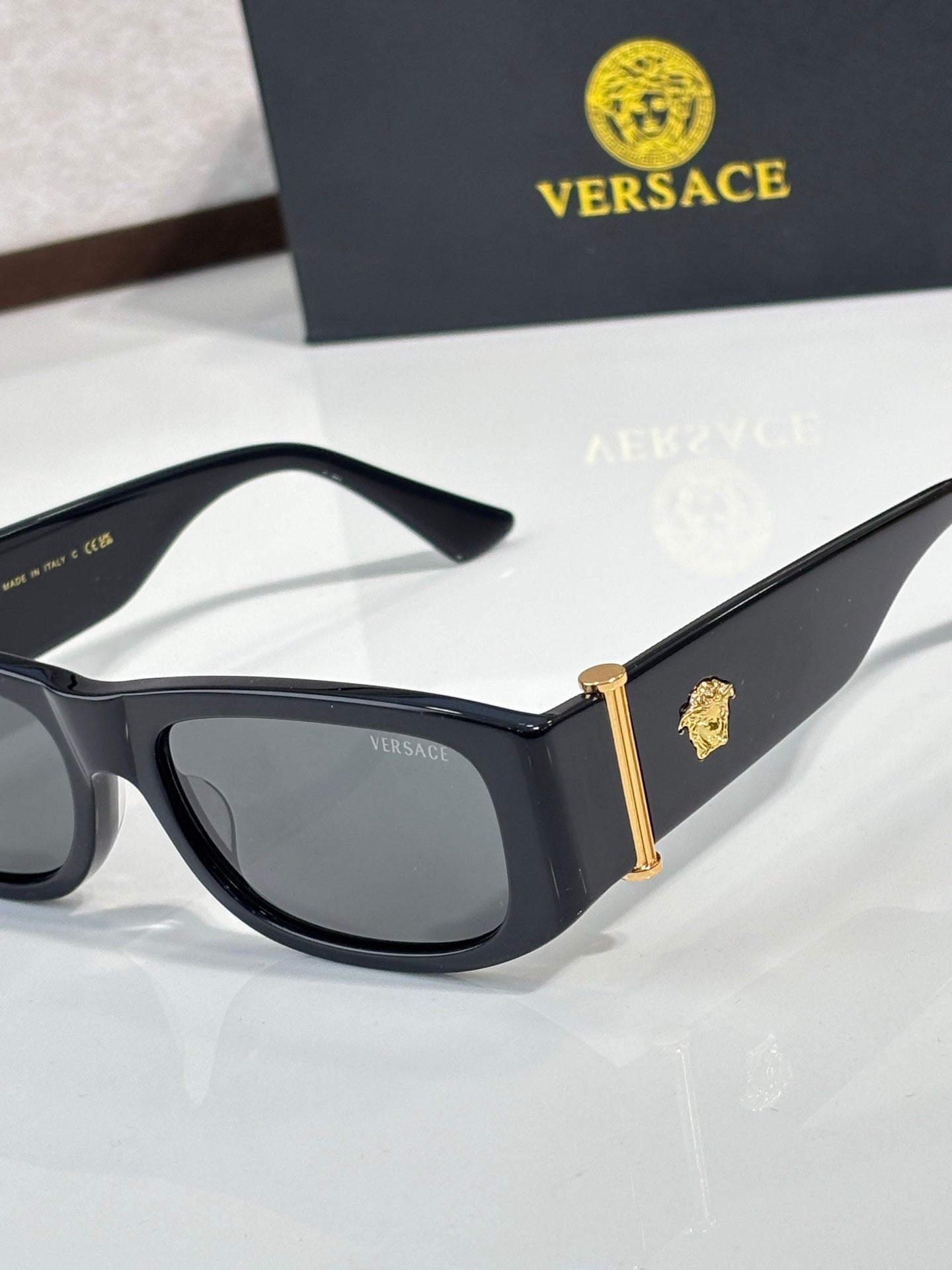 Versace sunglasses close-up with black frames and gold emblem on temples, dark lenses