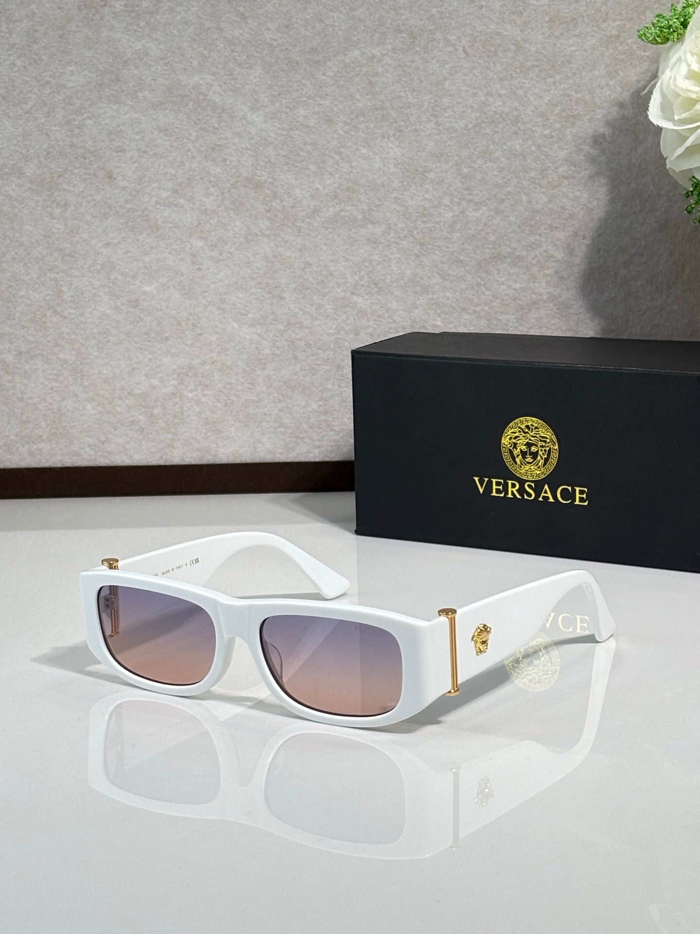 Versace sunglasses with white frames, gold temple accents, and light pink tinted lenses
