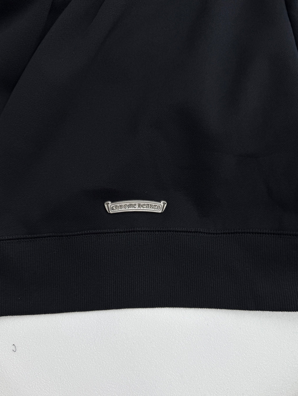Black sweatshirt hem with small oval brand patch label