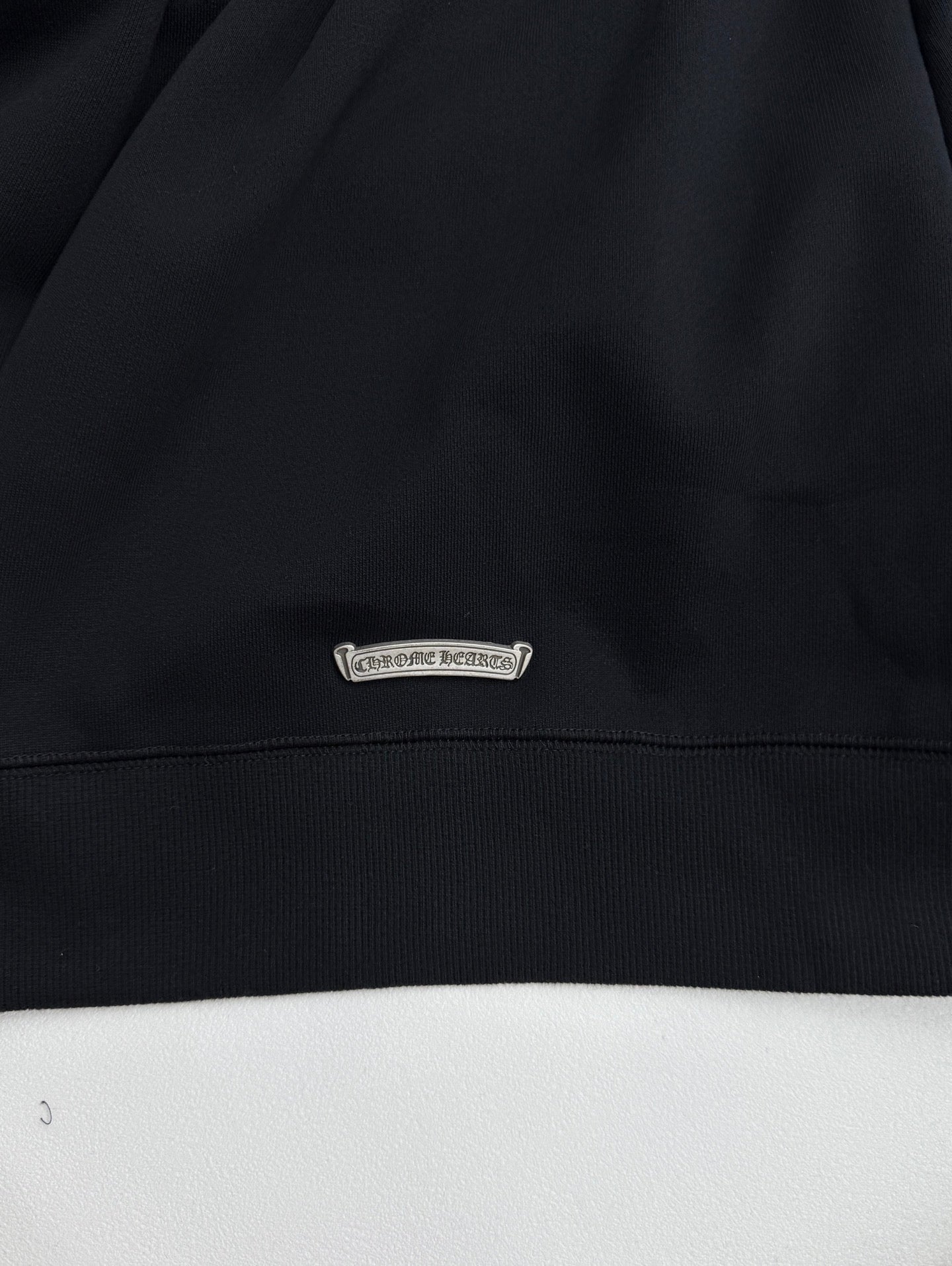 Black sweatshirt hem with small oval brand patch label