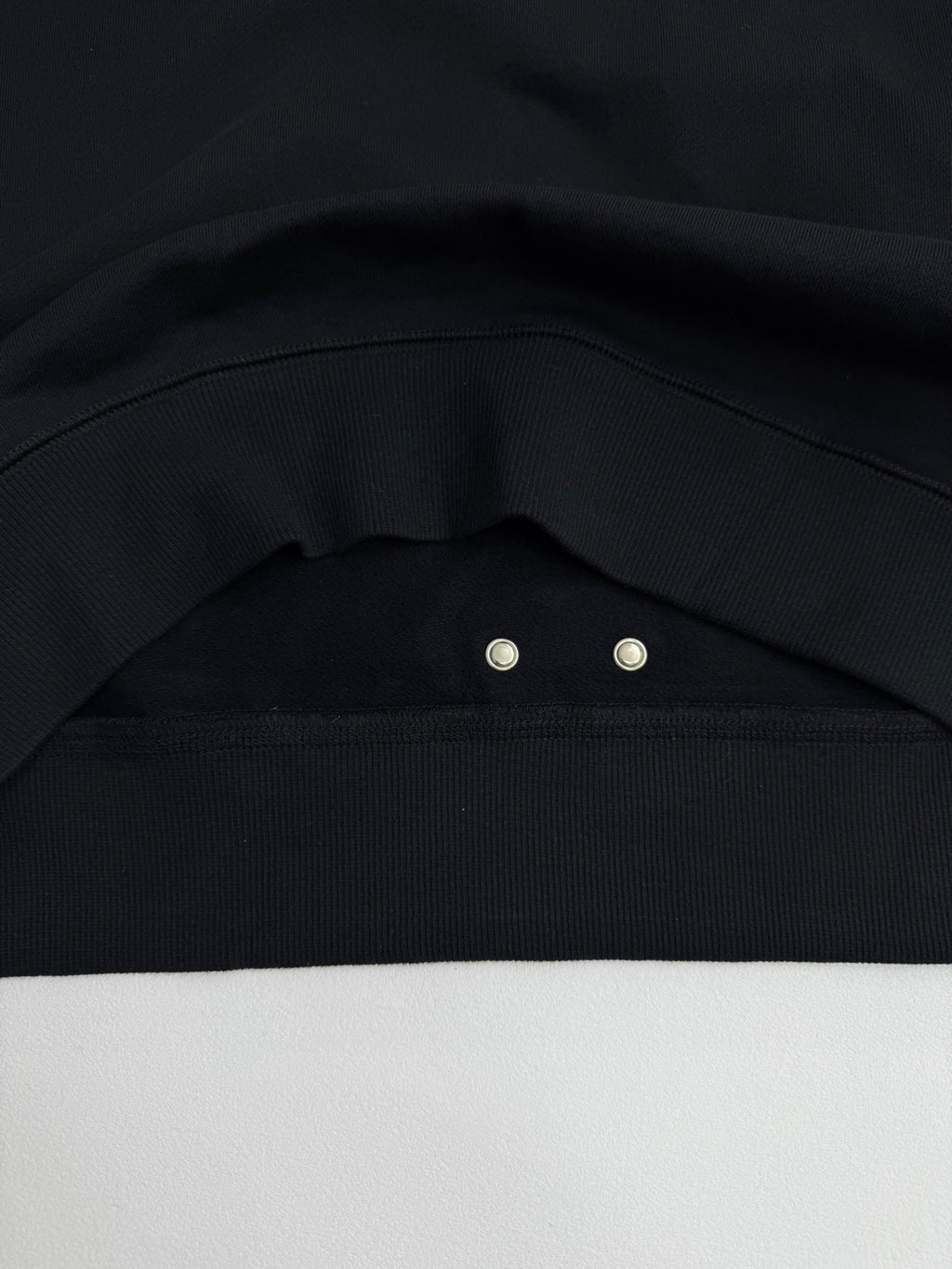 Black sweatshirt shoulder seam with metal snap at the collar