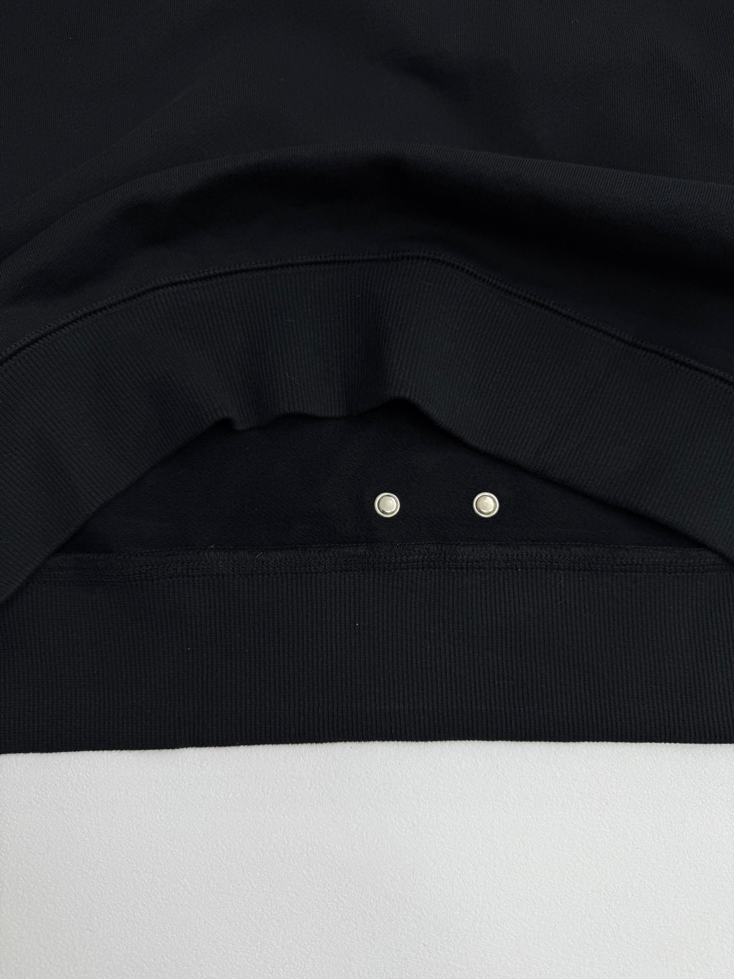 Black sweatshirt shoulder seam with metal snap at the collar
