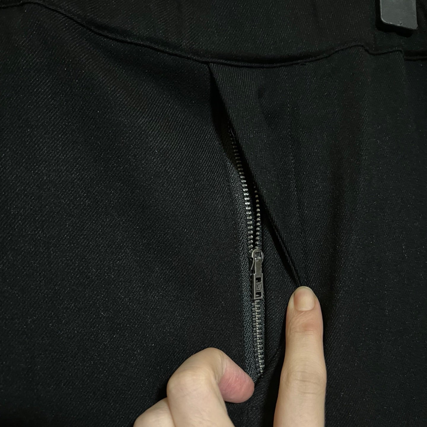 Black pants zipper detail with hand pulling closed fly