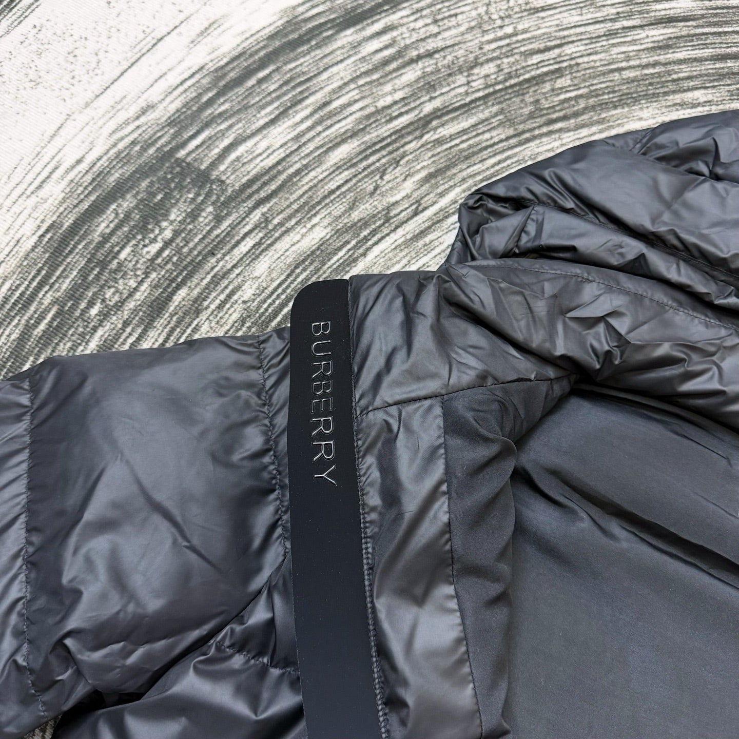 Dark puffer jacket shoulder panel with vertical Burberry logo tab