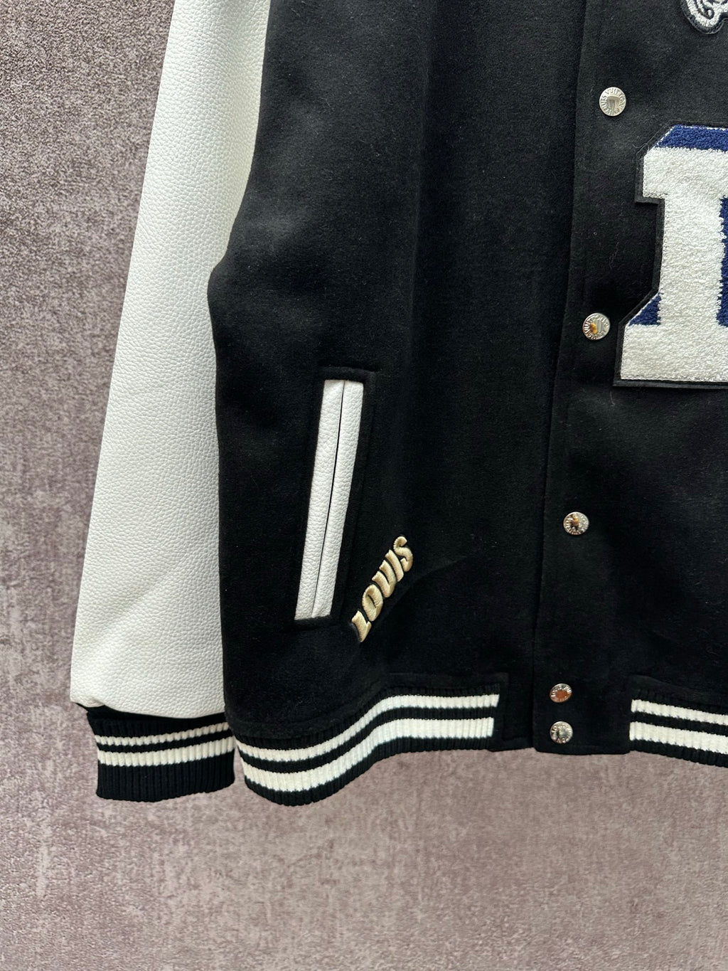 Black varsity jacket sleeve and hem with white stripe ribbing and gold-button placket