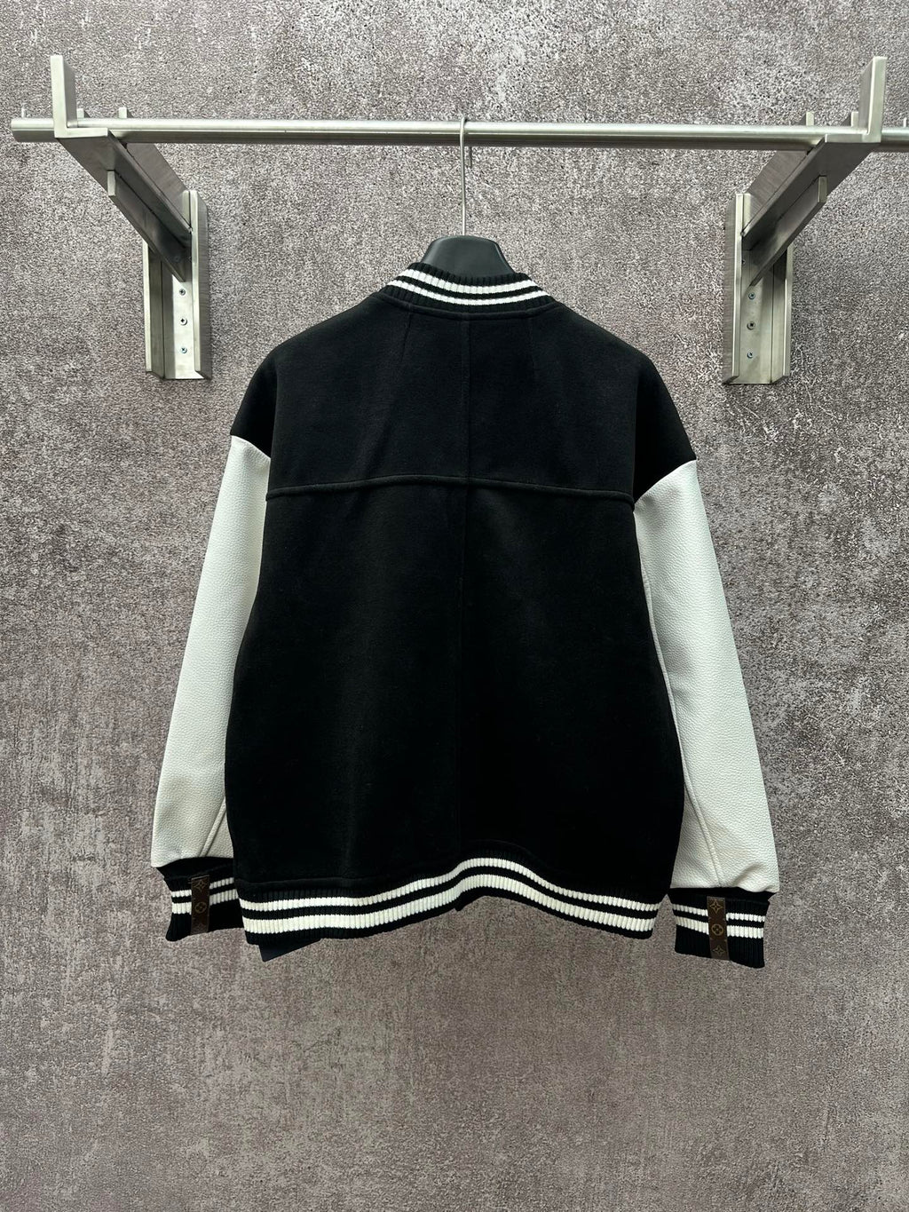 Back view of black long varsity jacket with white sleeve panels and ribbed hem