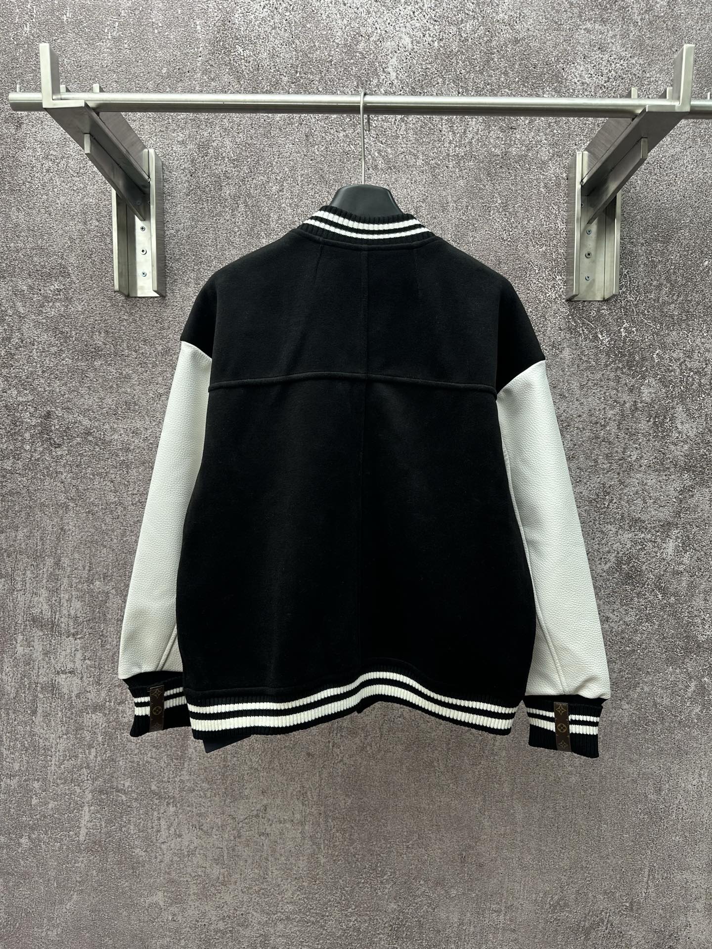 Back view of black long varsity jacket with white sleeve panels and ribbed hem