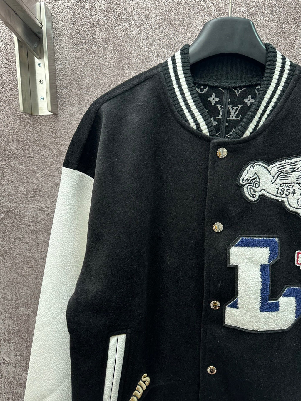 Black varsity jacket with white sleeves, button placket and crest graphic detail