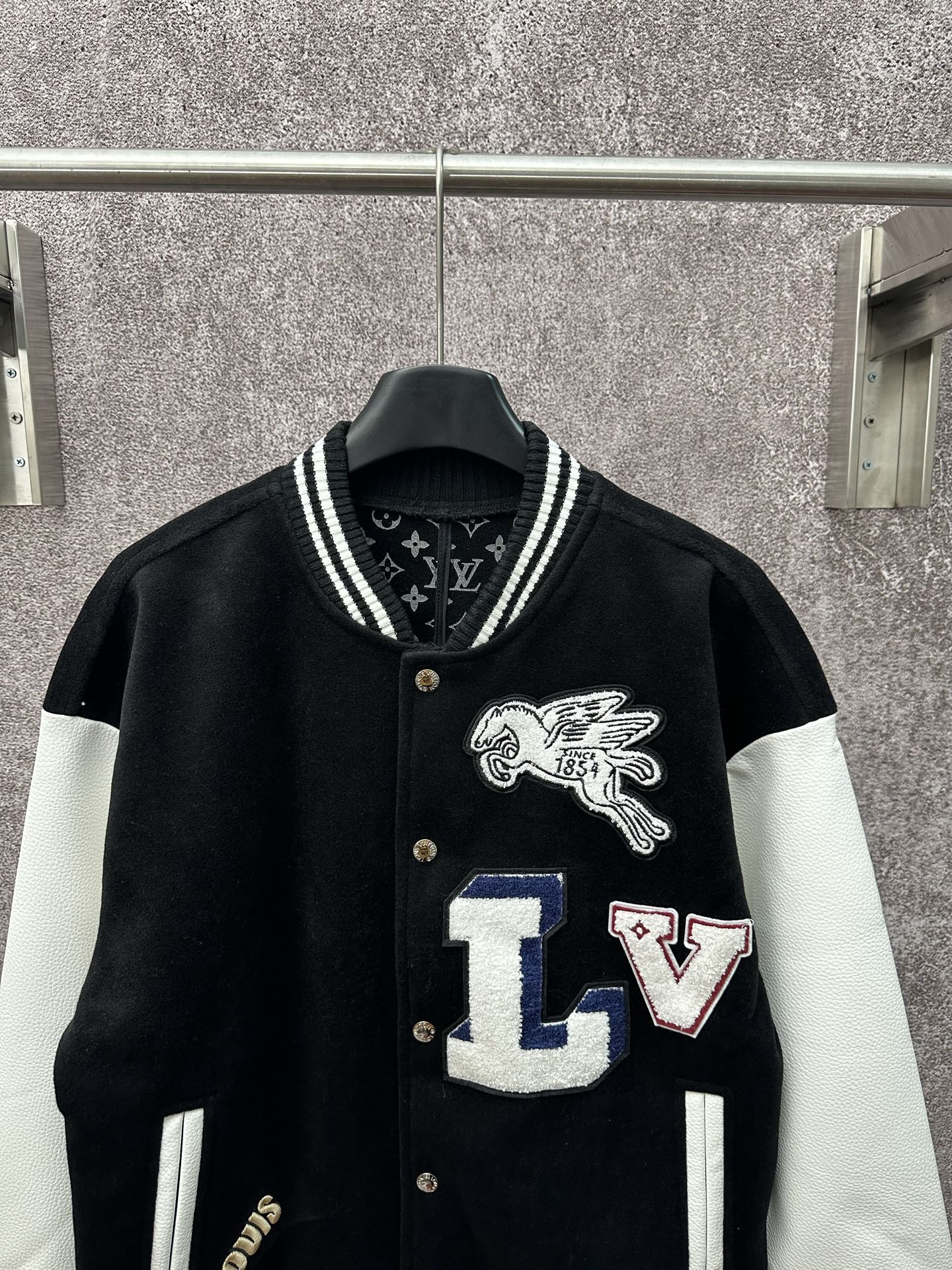 Black long varsity jacket with white sleeves, crest logo and LV letter patches on front