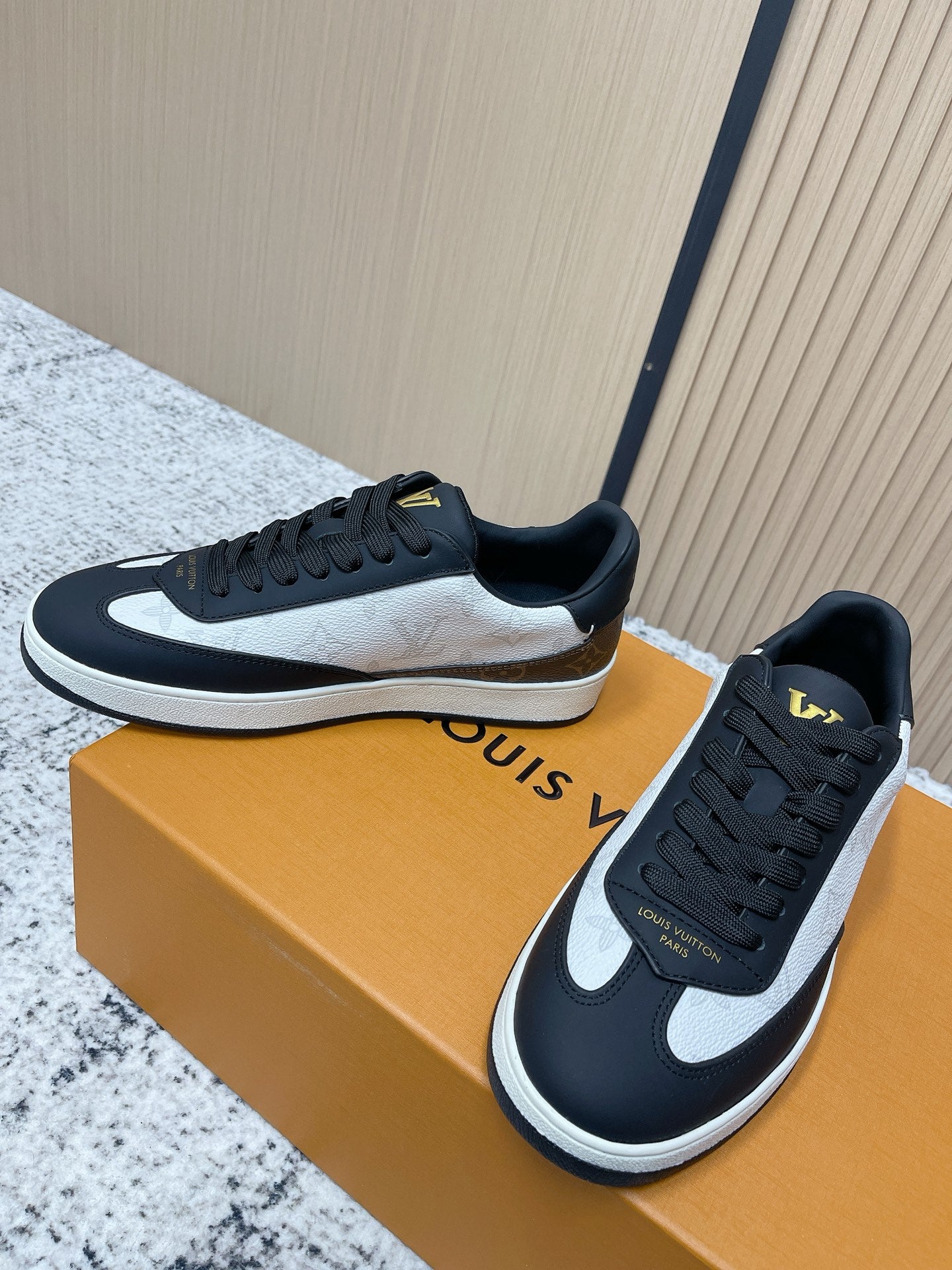 Louis Vuitton low-top sneakers with black laces, white midsole, gold LV on tongue