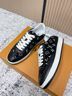 Black low-top sneakers with white laces and monogram-style print, side view on box.