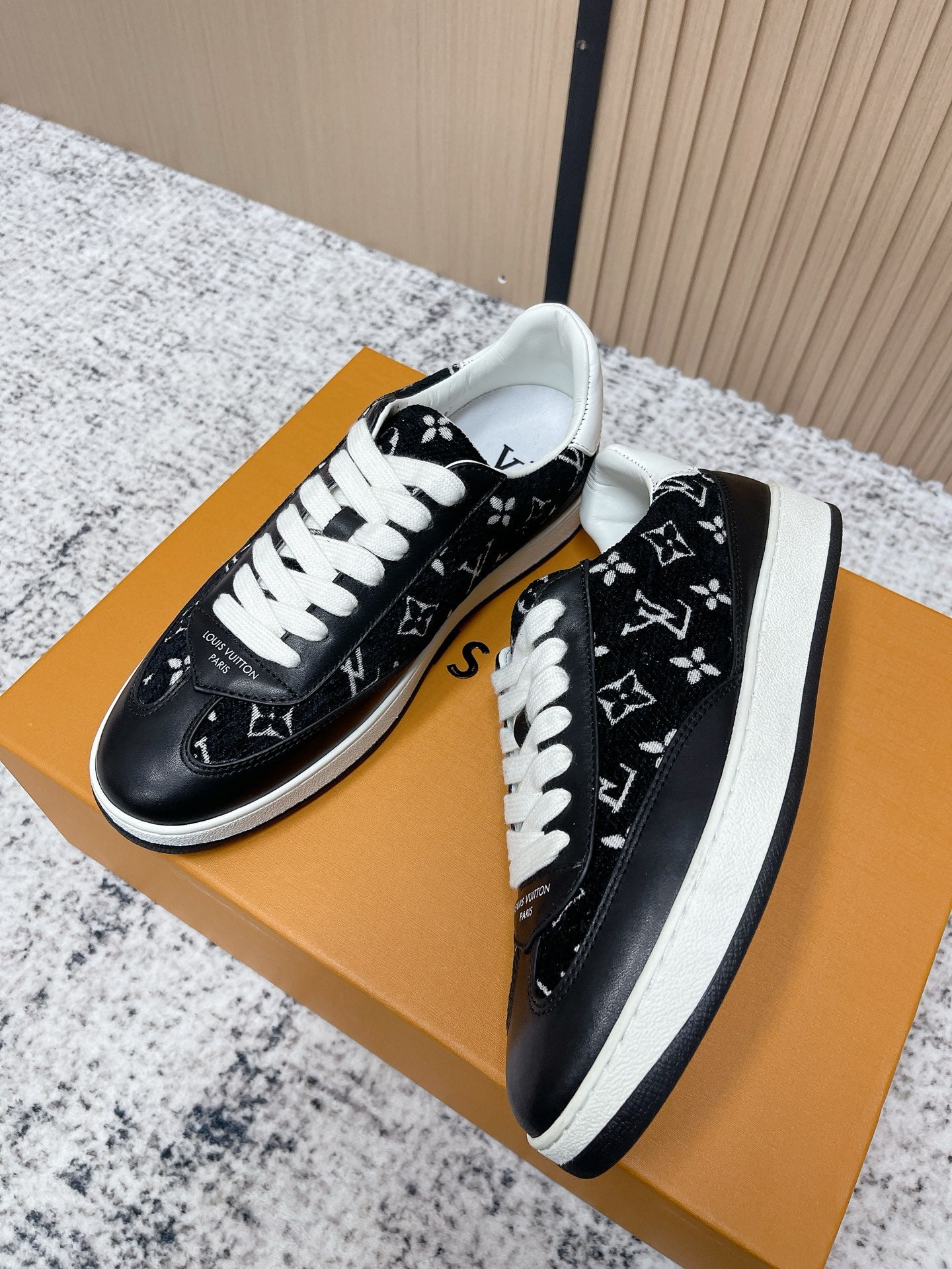 Black low-top sneakers with white laces and monogram-style print, side view on box.
